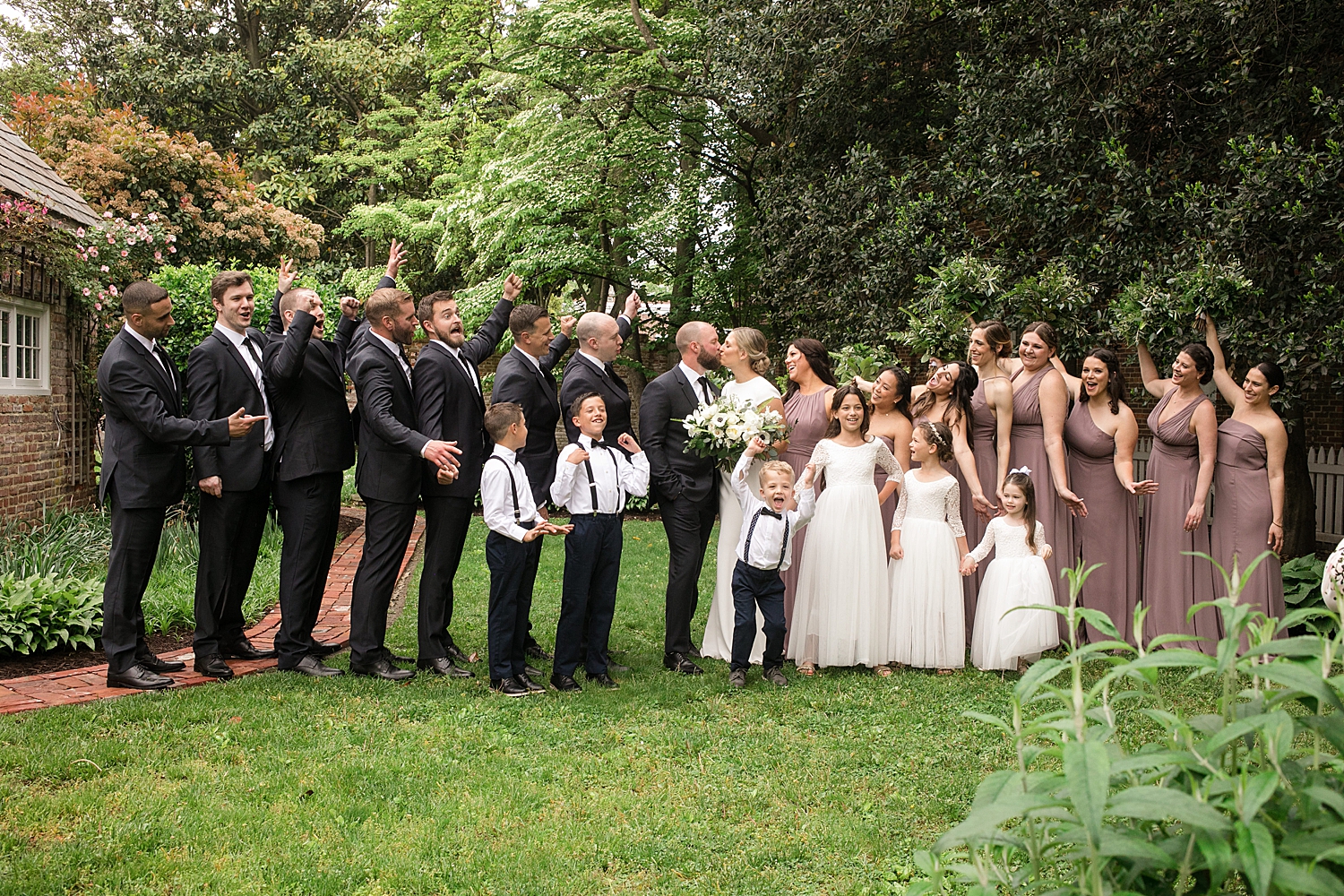 full wedding party celebrates while bride and groom kiss