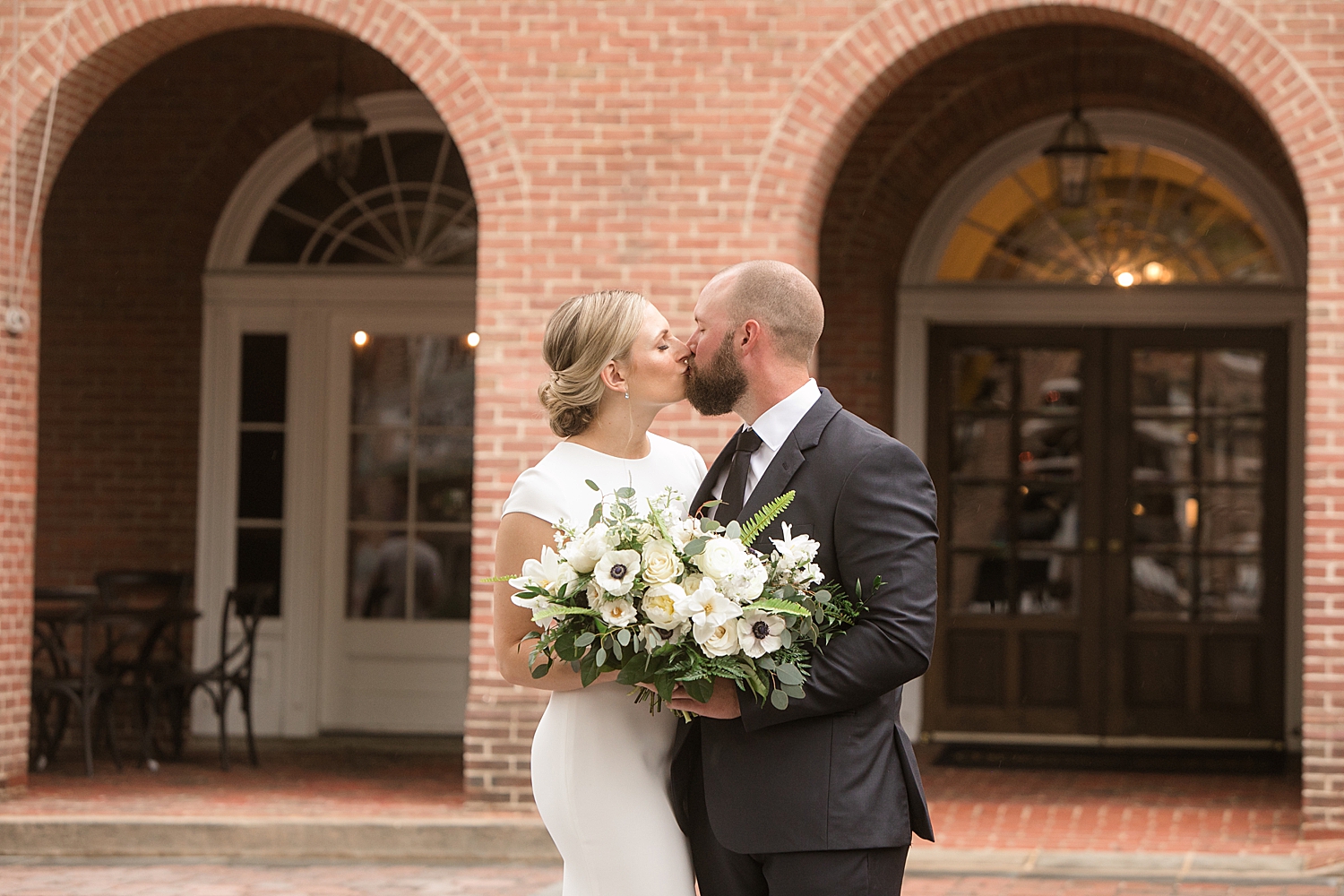 bride and groom kiss in front of brick arches