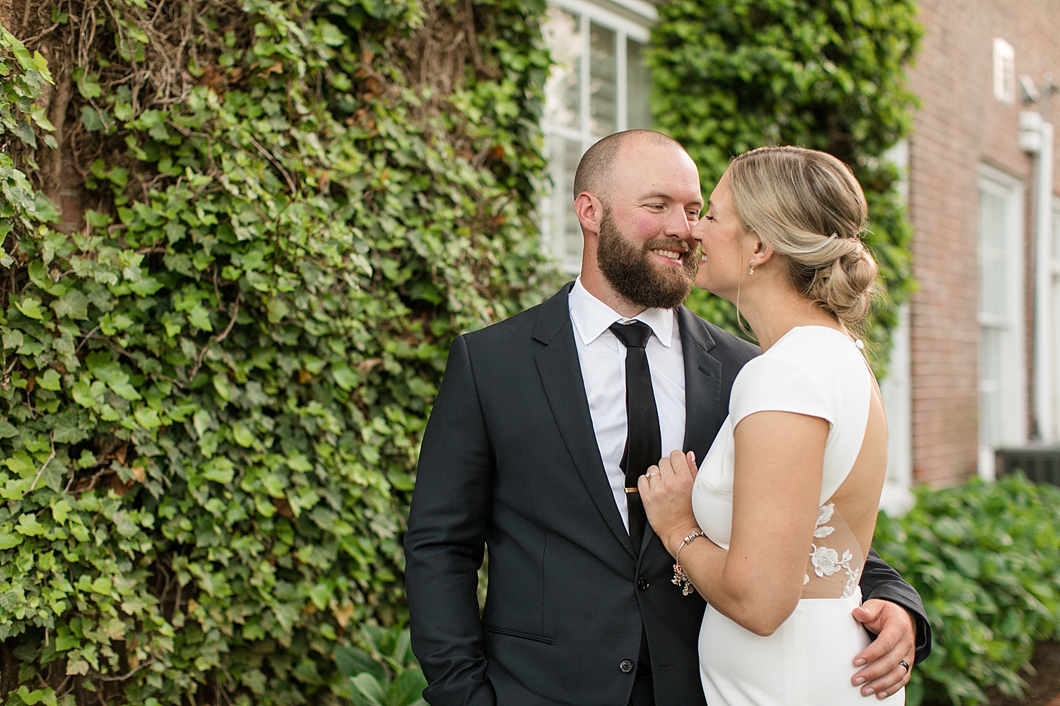 bride and groom embrace in front of brick wall covered in ivy