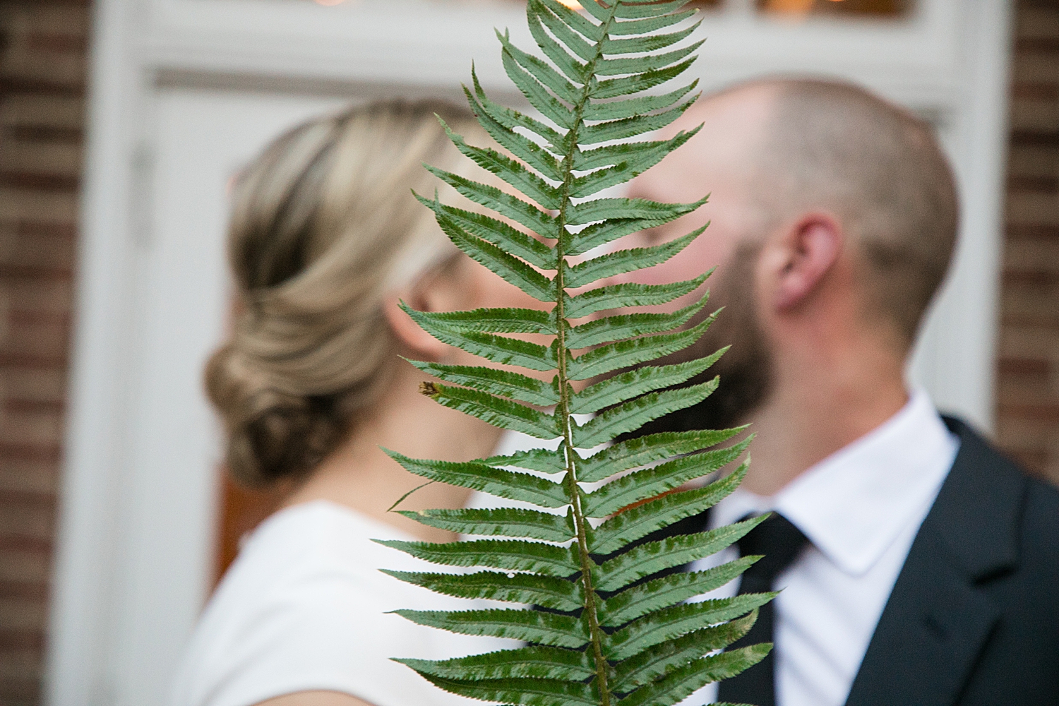 bride and groom kiss behind a leather fern