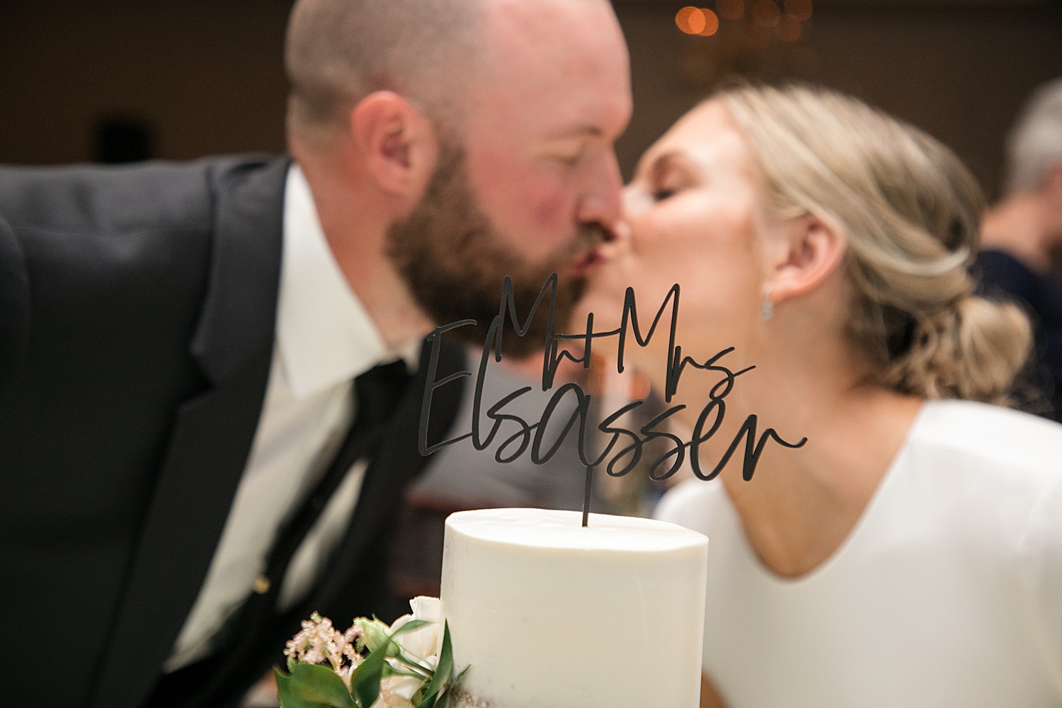 bride and groom kiss behind cake topper with new last name