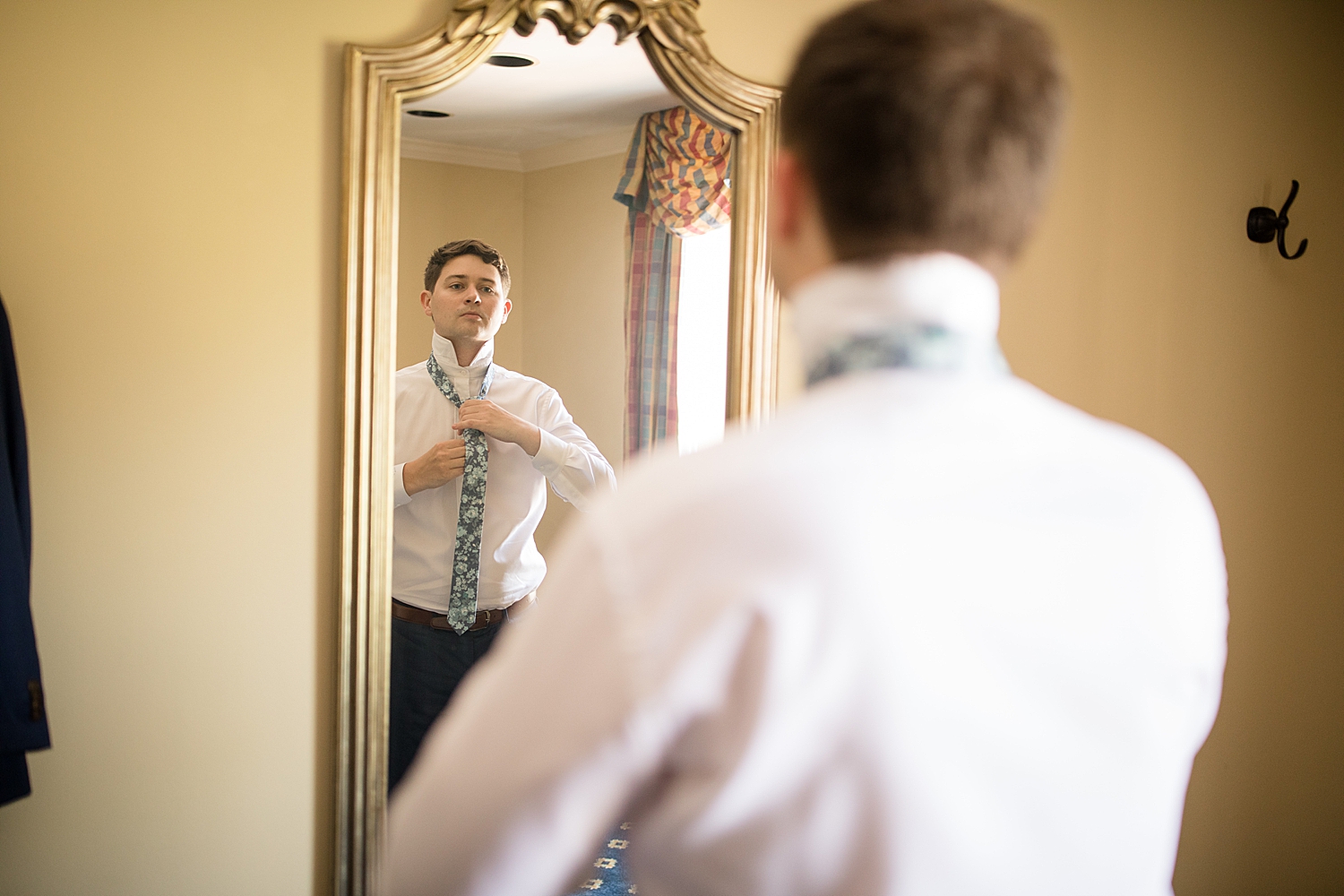 groom getting ready, tying tie in mirror