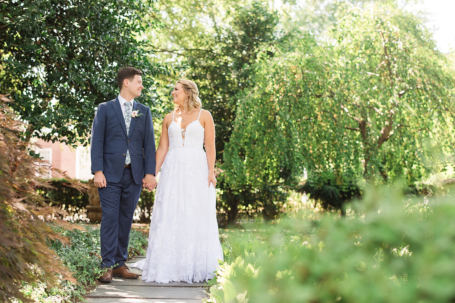 bride and groom walk along garden-lined path