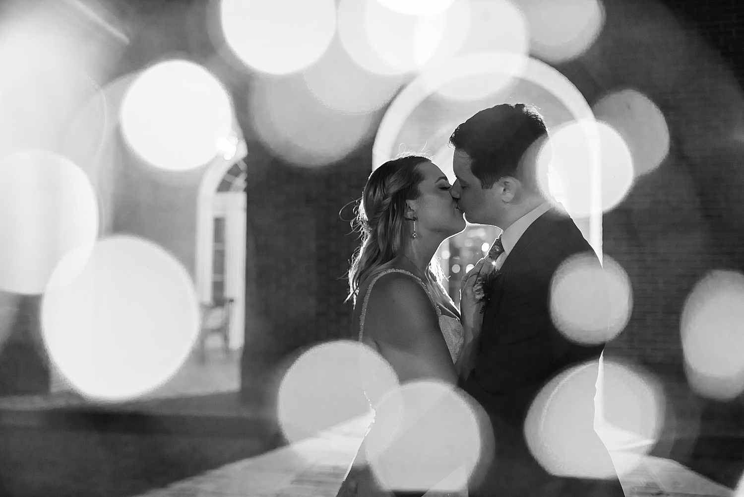 black and white bride and groom kiss with bokeh