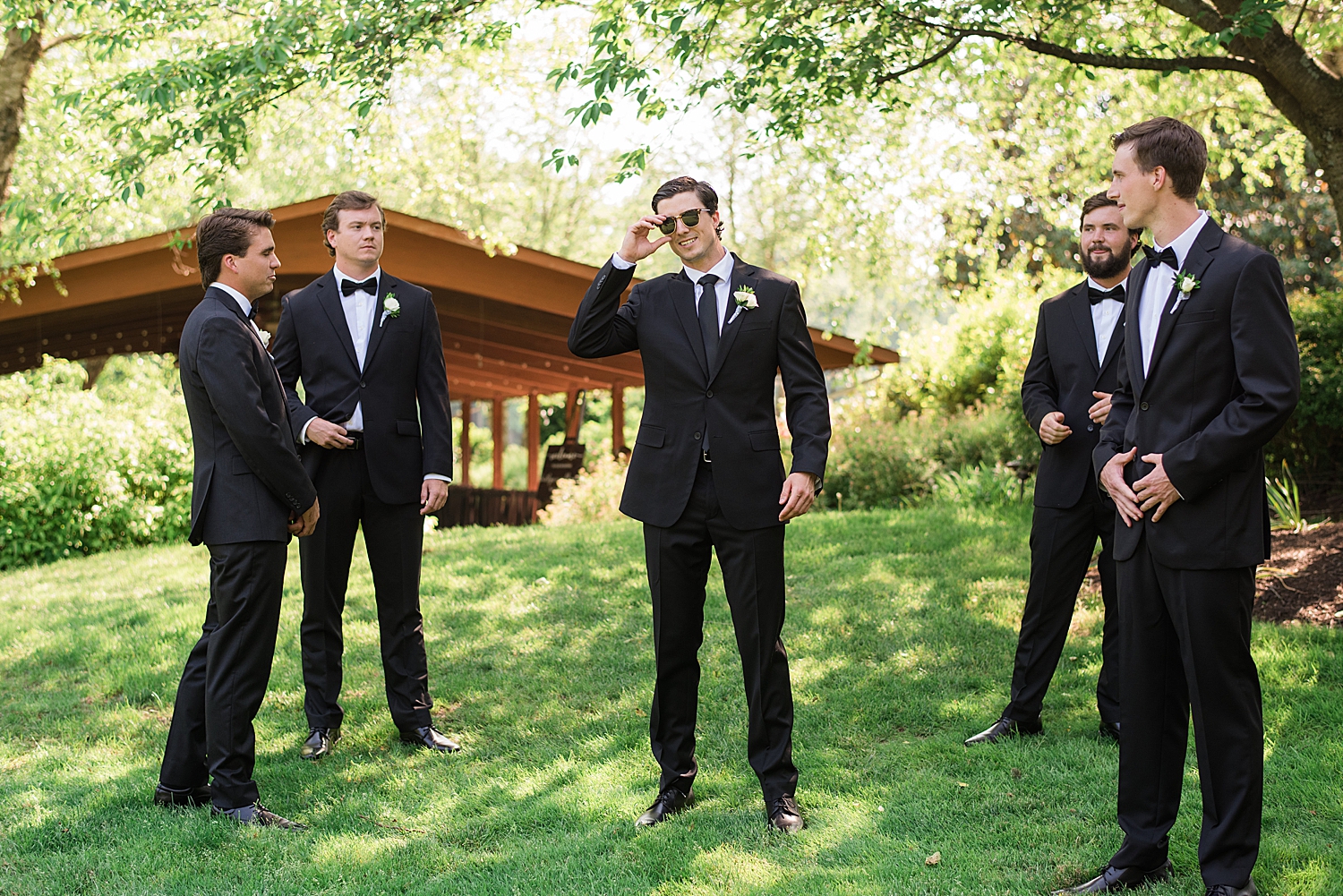 groomsmen looking on while groom poses with sunglasses