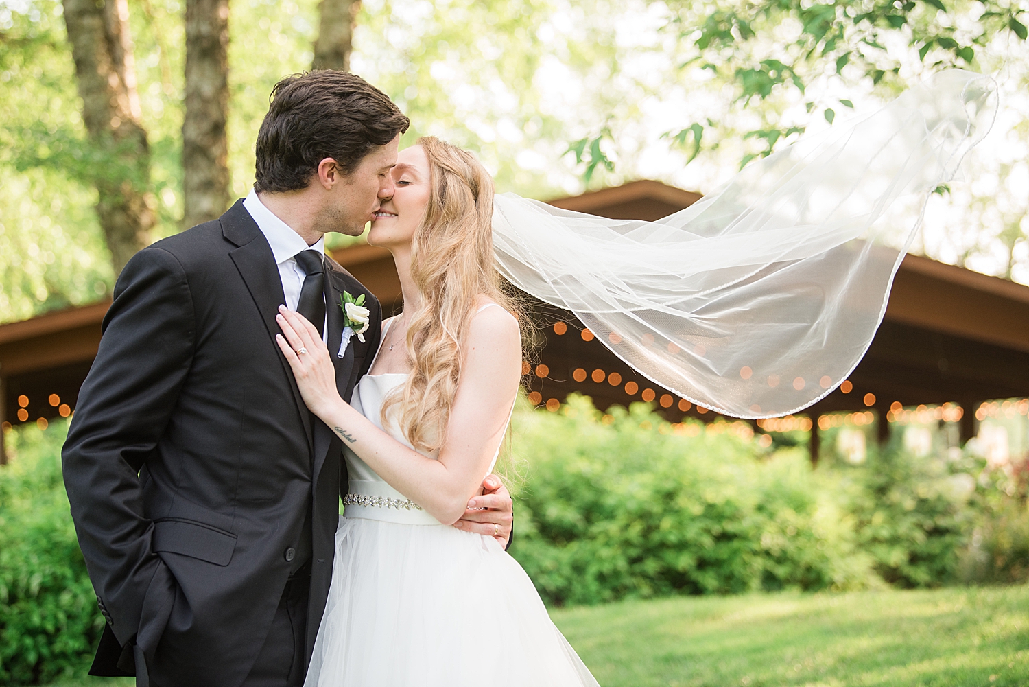 bride and groom kiss, veil blows in wind