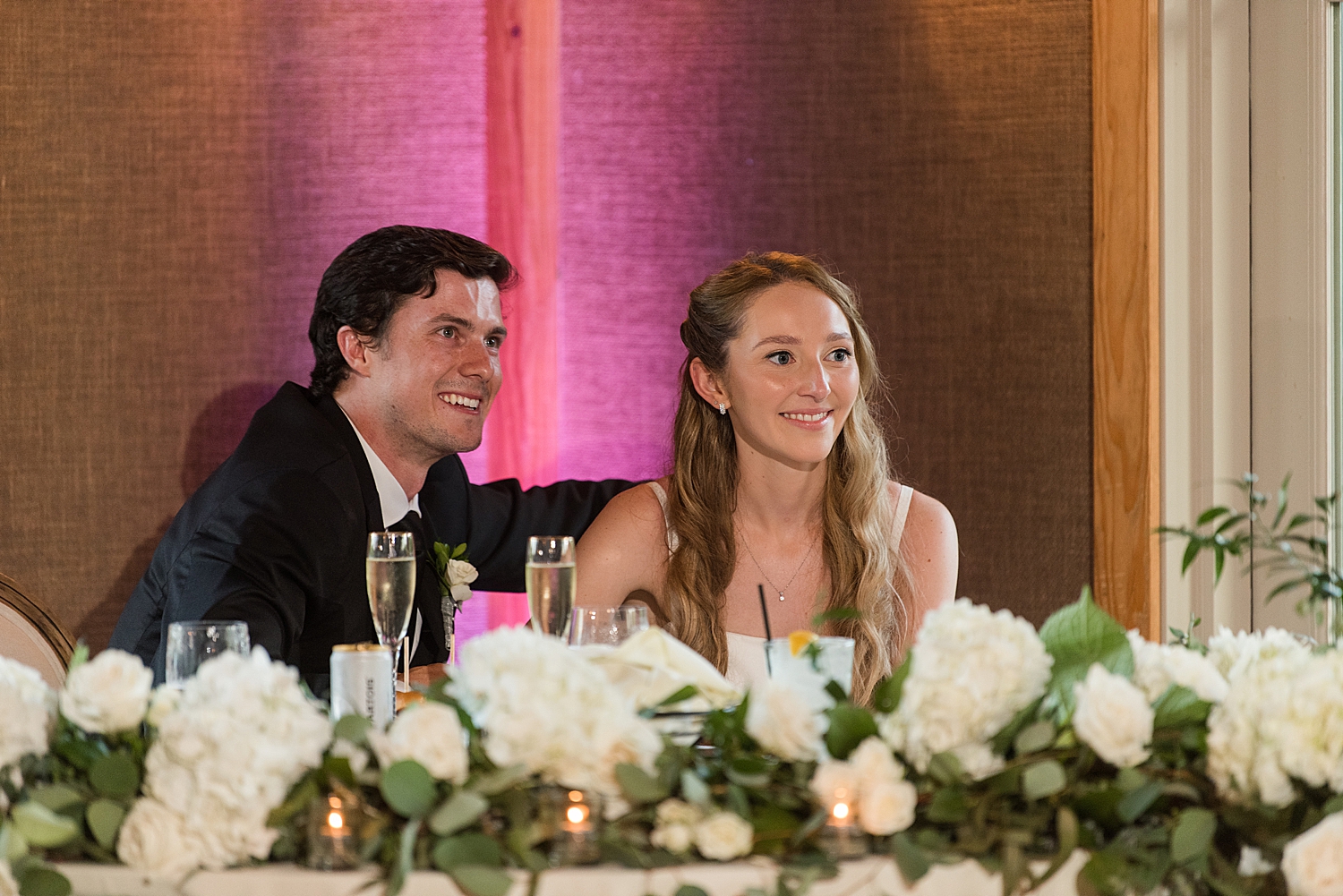 bride and groom sit at sweetheart table and smile at toast