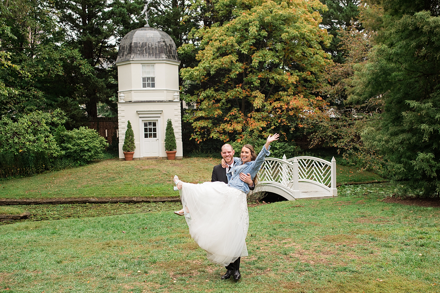 groom holds bride, kicking her feet up in denim jacket