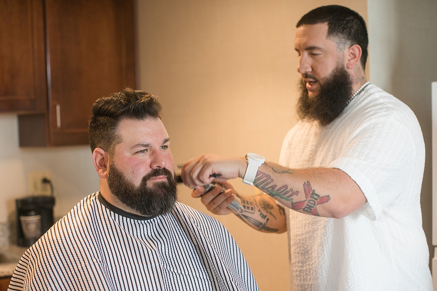 groom getting beard shaped by tattooed barber