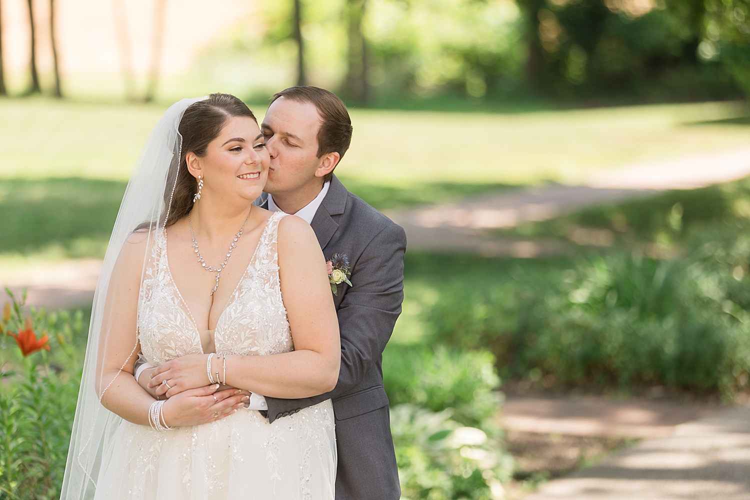 groom embraces bride from behind, kisses cheek