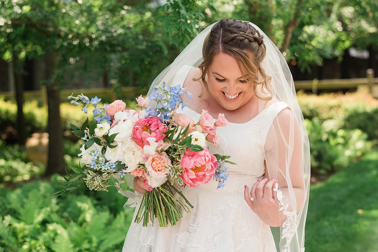 bride holds big pink and blue summer bouquet and laughs