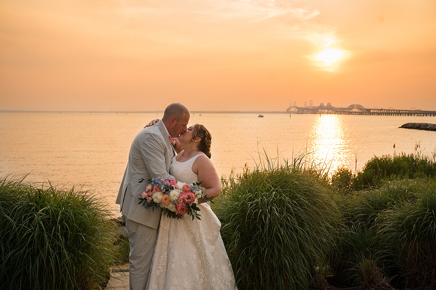 bride and groom kiss in front of bay at sunset