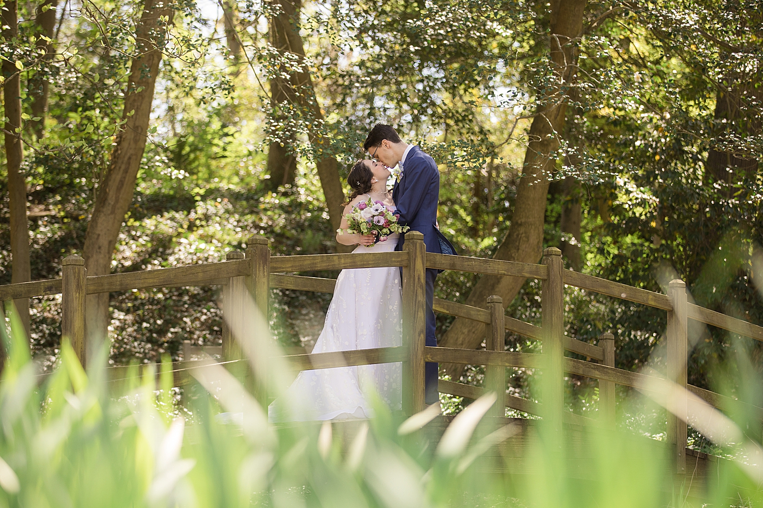 bride and groom kiss on bridge among the trees