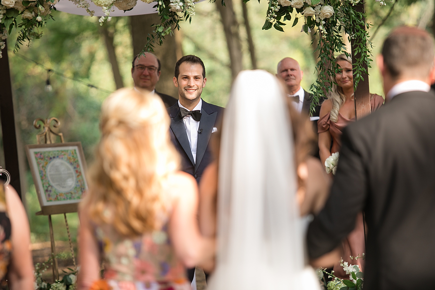 groom's face over bride's shoulder as she walks down the aisle