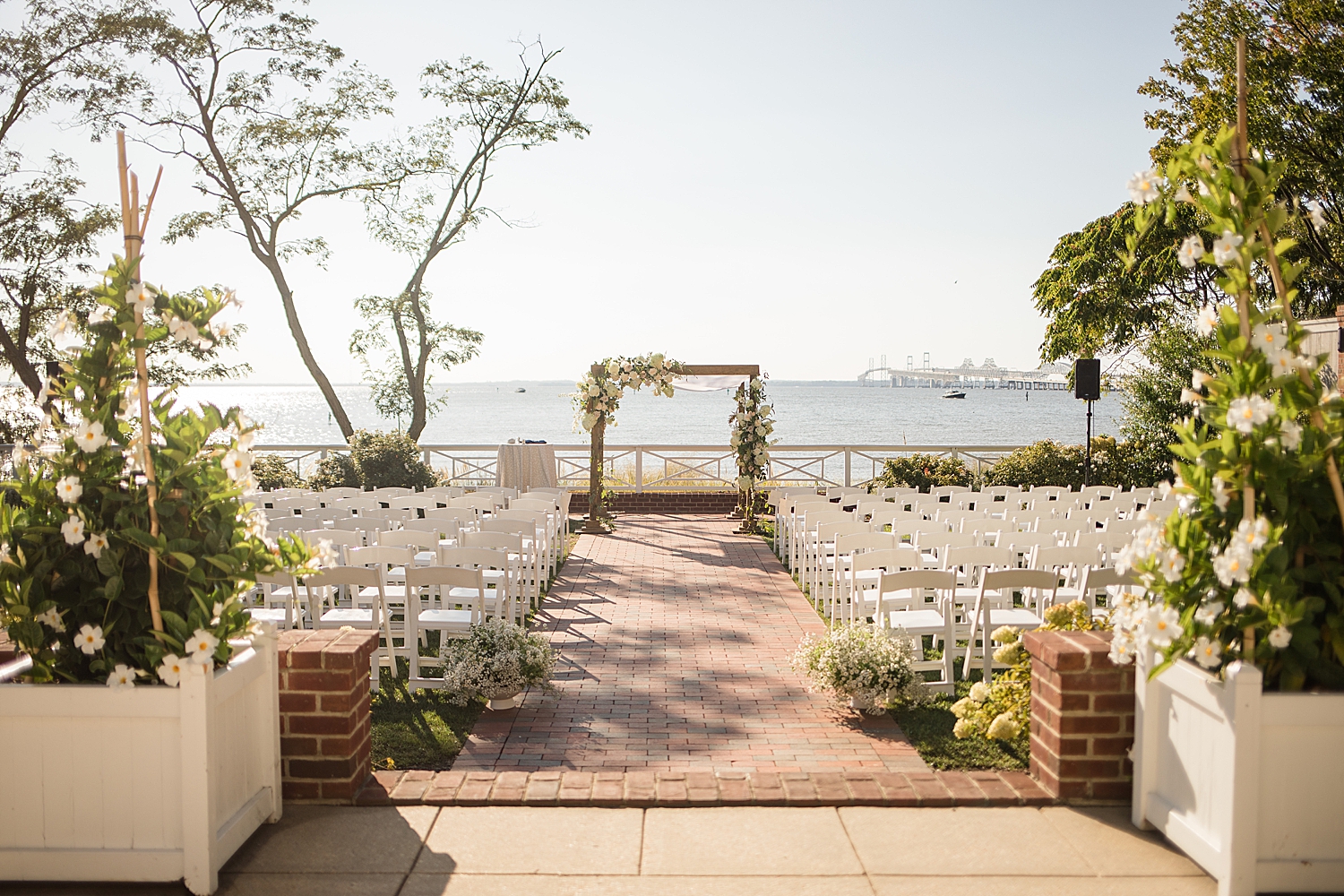 wide shot ceremony setup white floral arch on bay