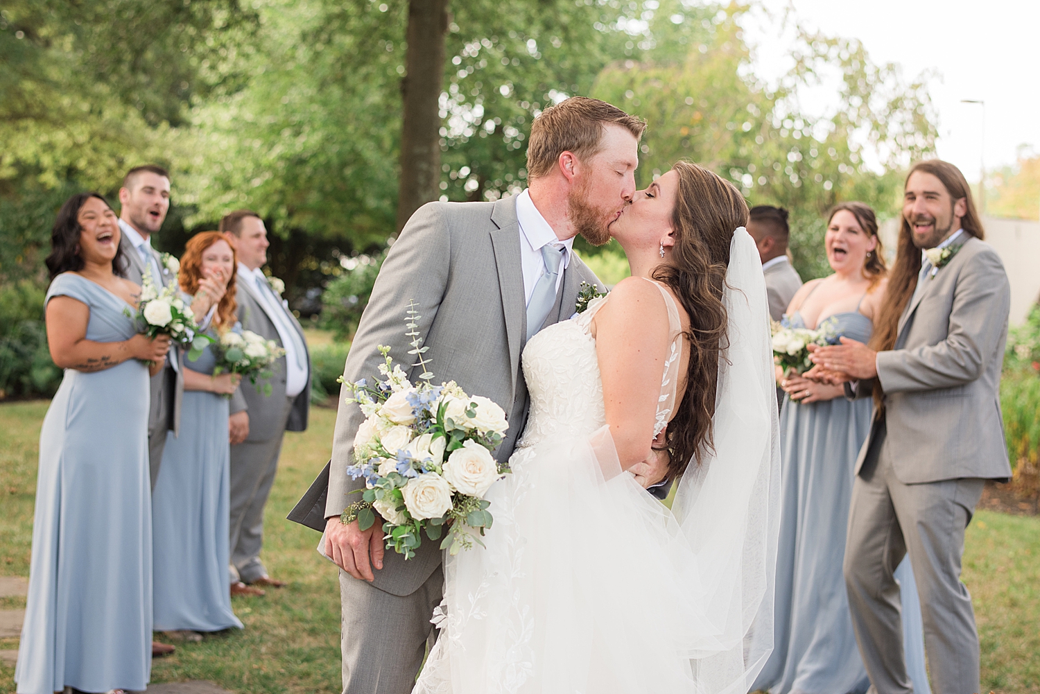 bride and groom kiss surrounded by wedding party