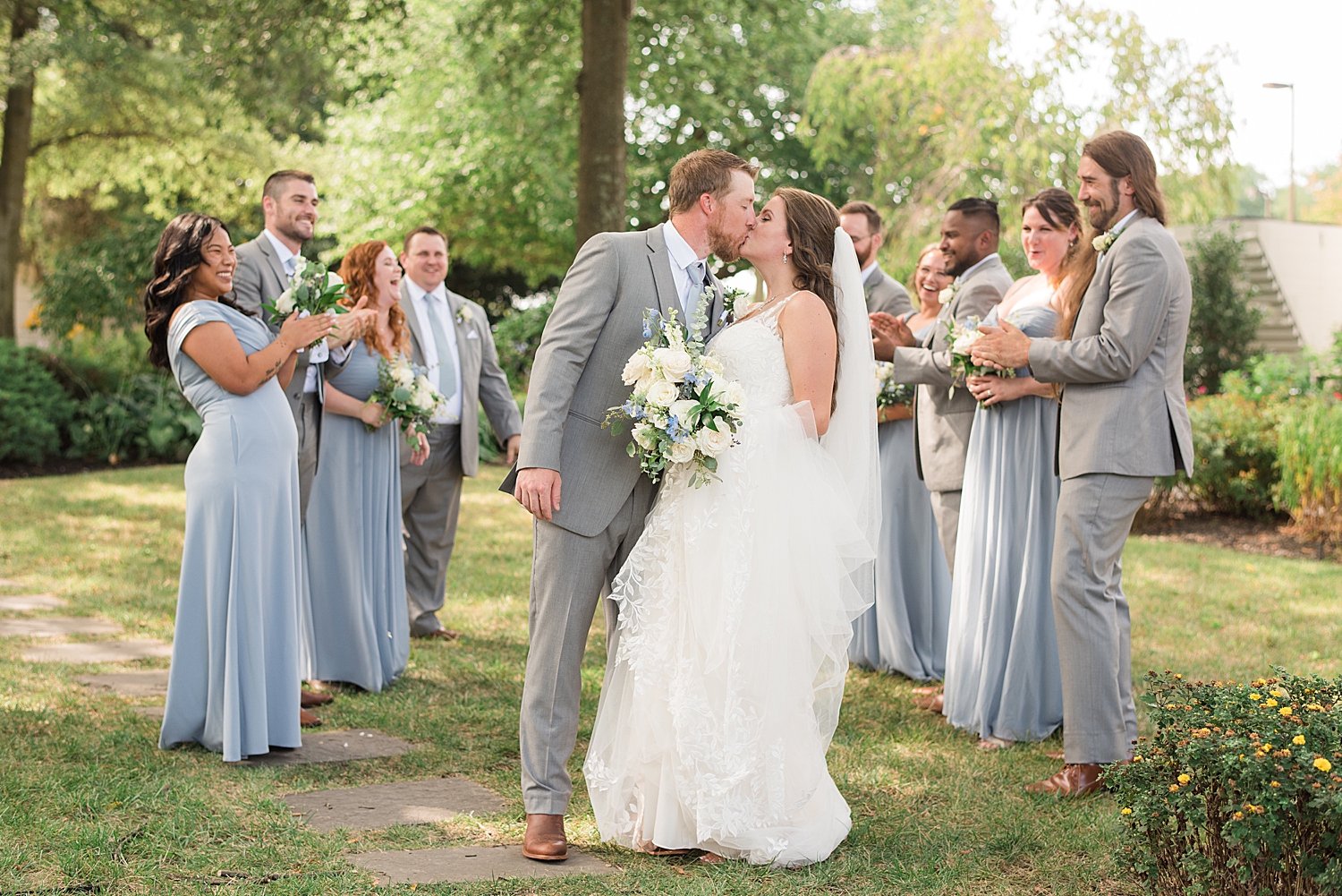 bride and groom kiss surrounded by wedding party