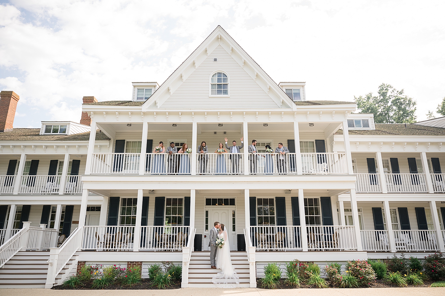 wide shot of kent island resort with wedding party on balcony and bride and groom on stairs