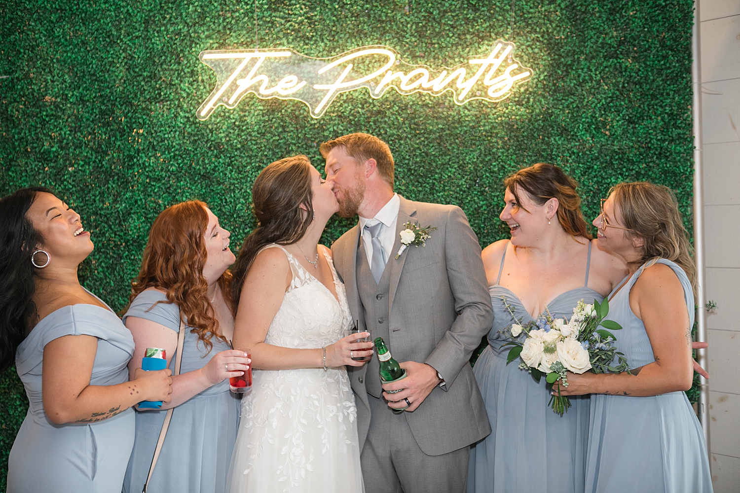 bride and groom kiss under neon sign of last name