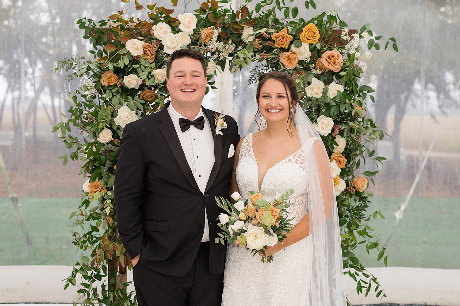 bride and groom smile in front of floral ceremony arch