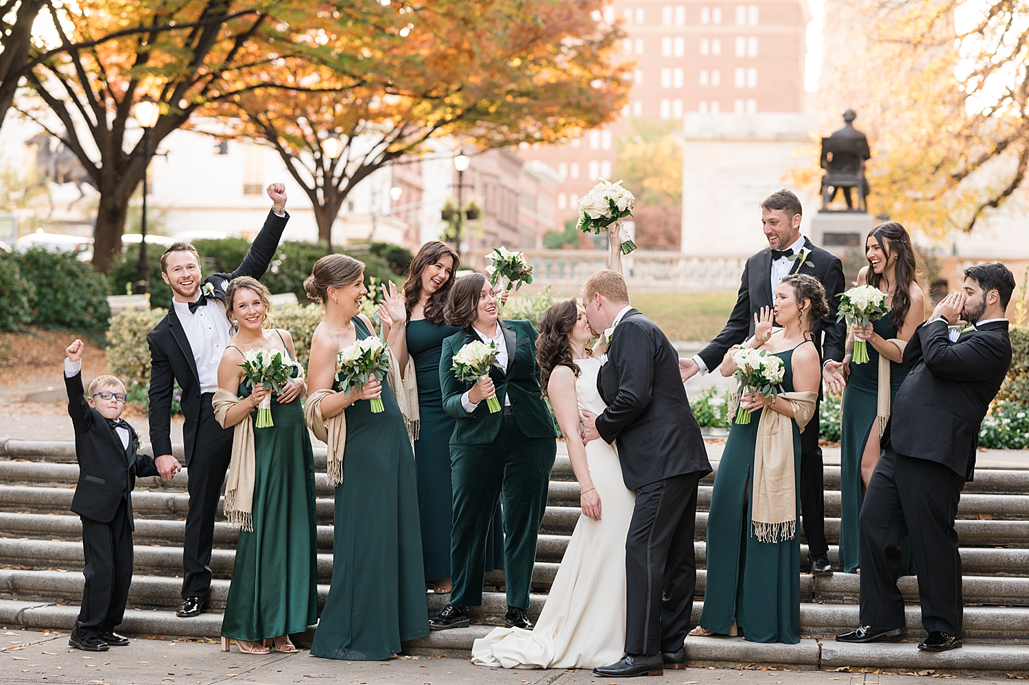 wedding party in black suits and emerald dresses couple kissing