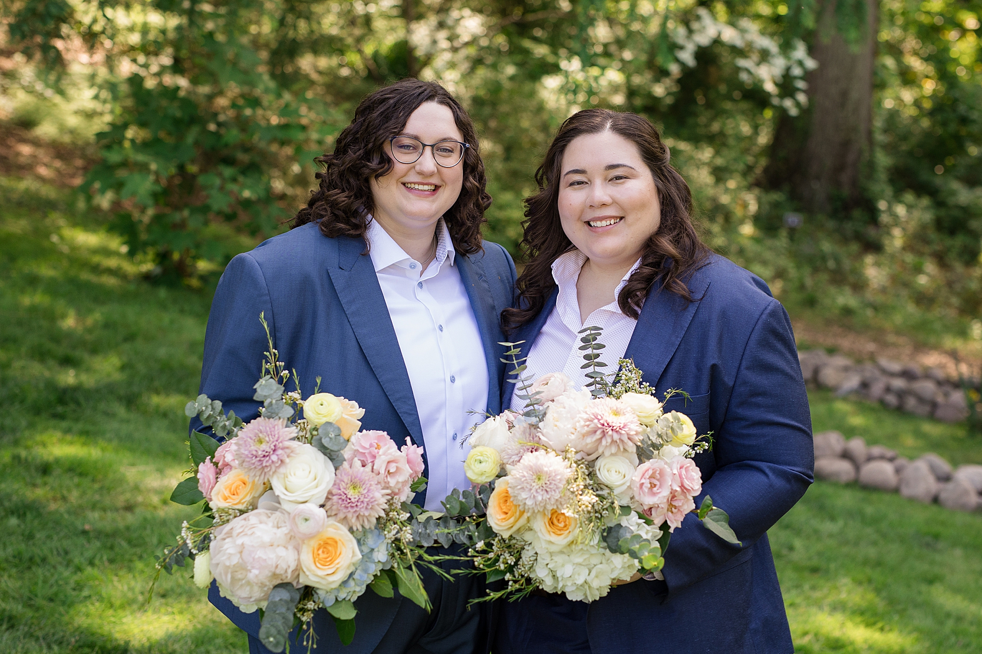two brides in a navy suit with two soft pink cream peach wedding bouquet