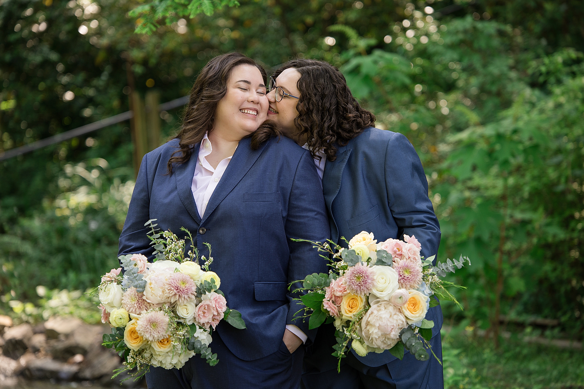two brides in a navy suit with two soft pink cream peach wedding bouquet
